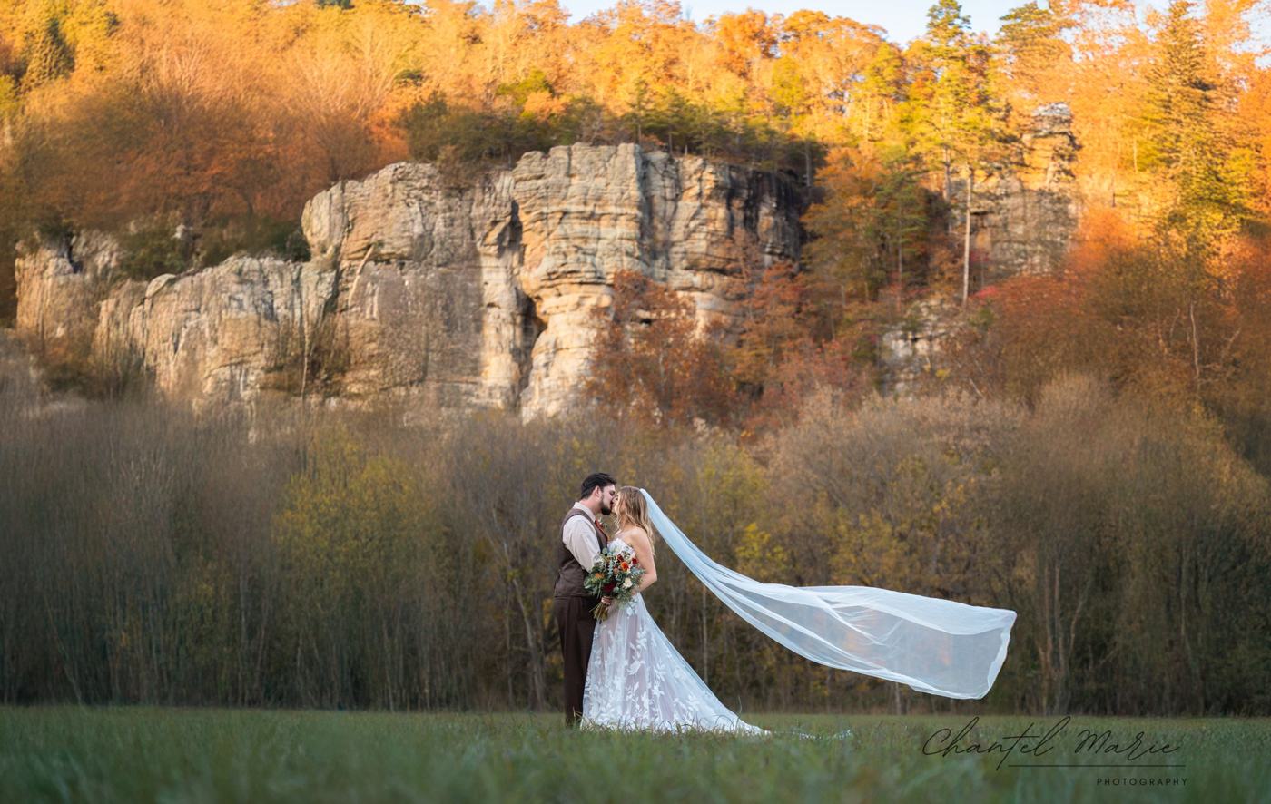 Bride and groom kissing beneath autumn cliffs with a flowing veil
