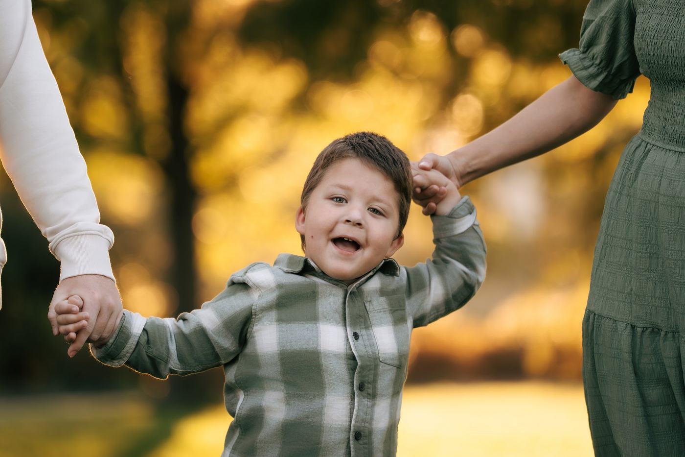 Child laughing while holding two adults’ hands outdoors
